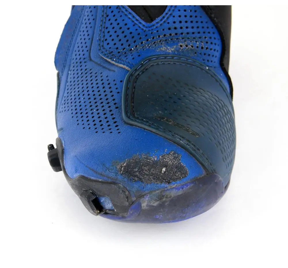 תקריב שחיקה עמוקה בעור הכחול של מגף רכיבה Alpinestars לפני עבודת שיקום
